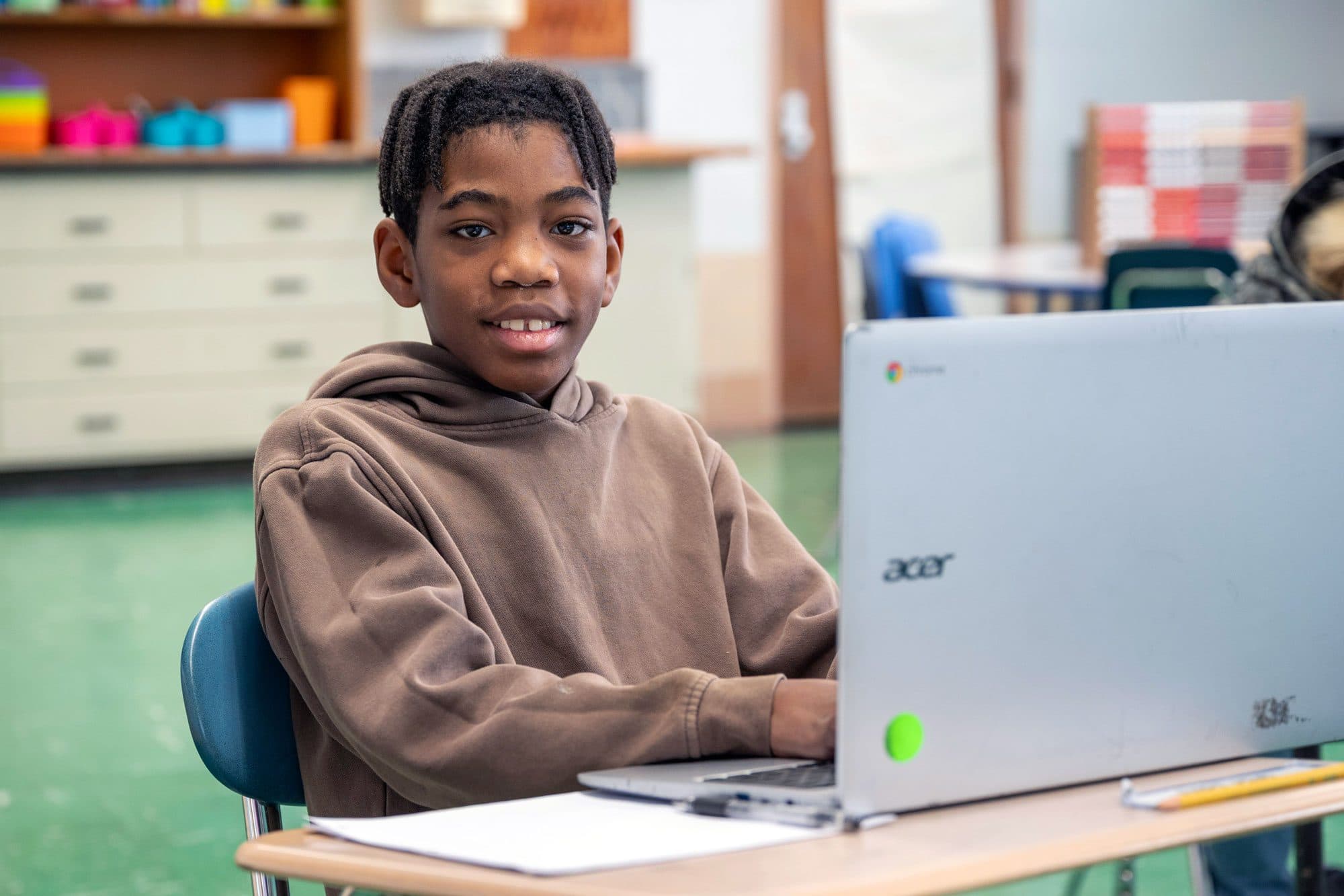 Smiling student using a laptop at a classroom desk.