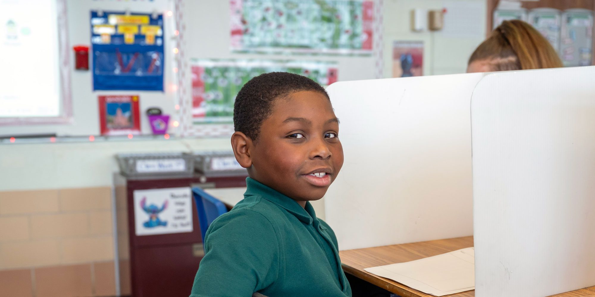 Student sitting at a classroom desk with a privacy shield.